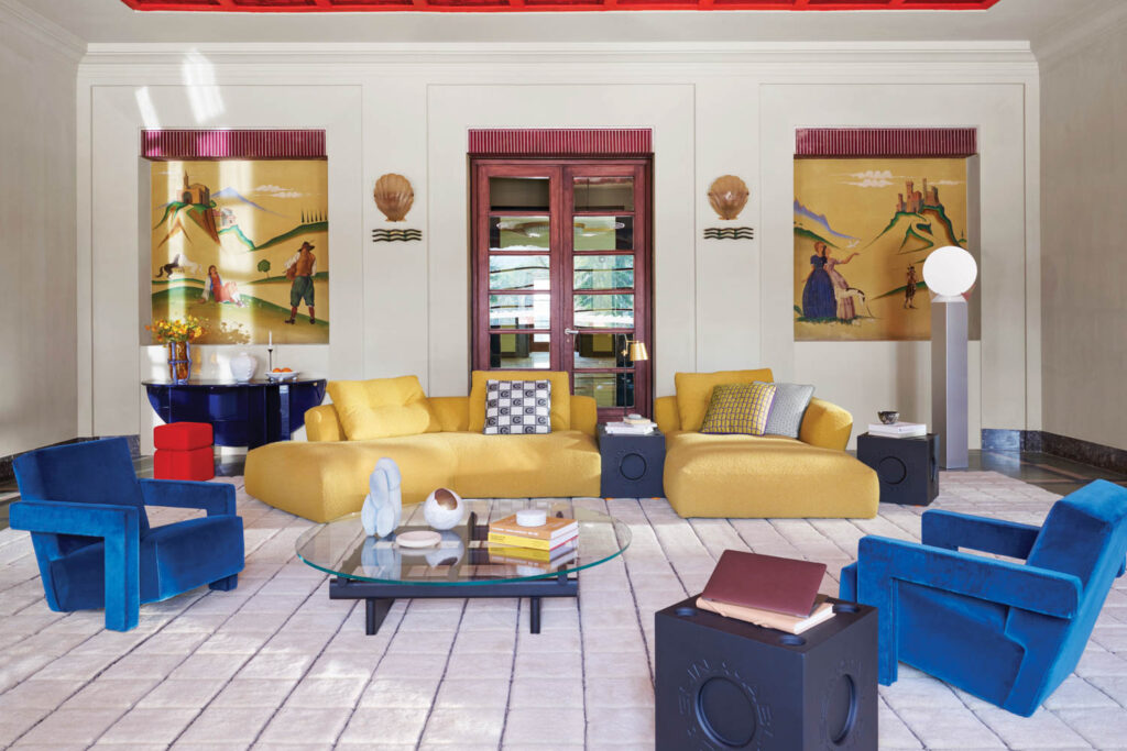 a living area with yellow couches, blue chairs, and the Modular Imagination cube by Cassina Abloh