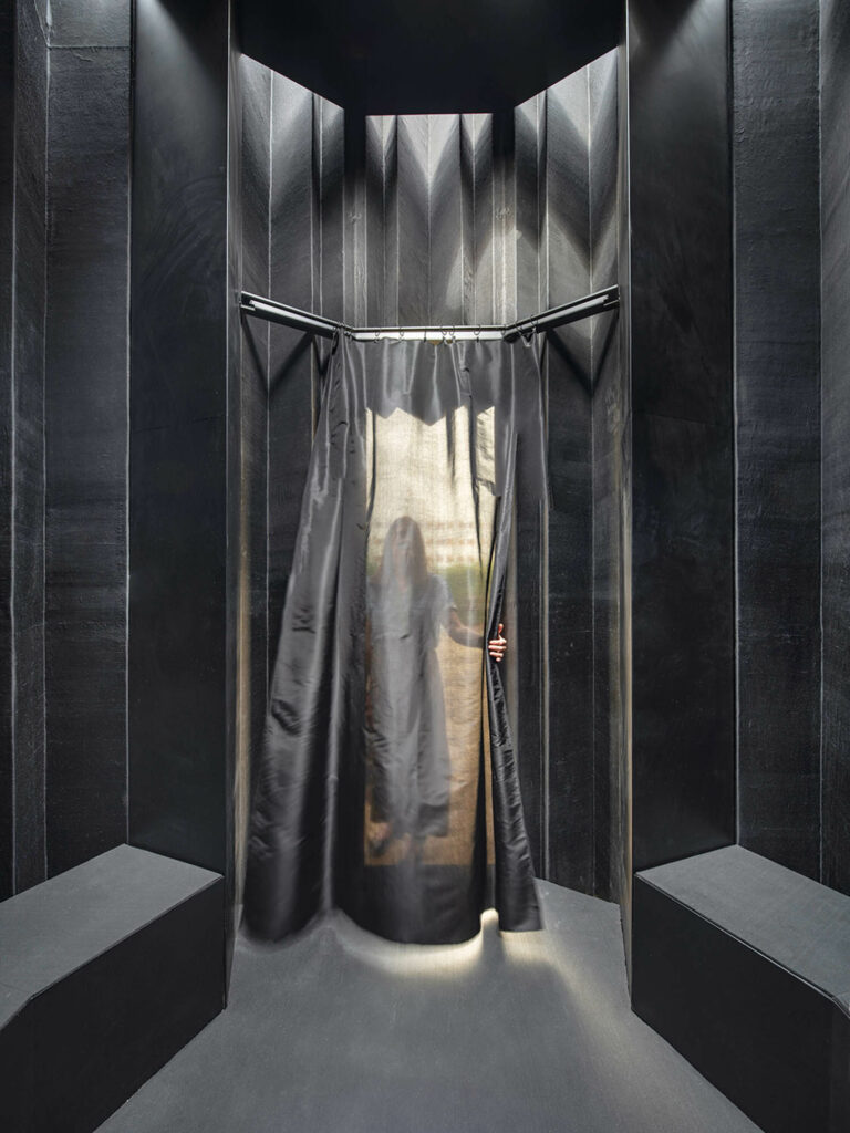 a sheer black curtain opens to black benches inside the Silk Pavilion